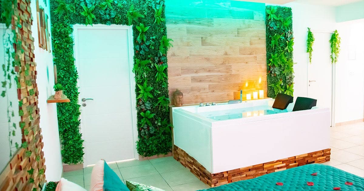 La baignoire balnéo deux places, encadrée de murs végétaux, avec sa base en bois