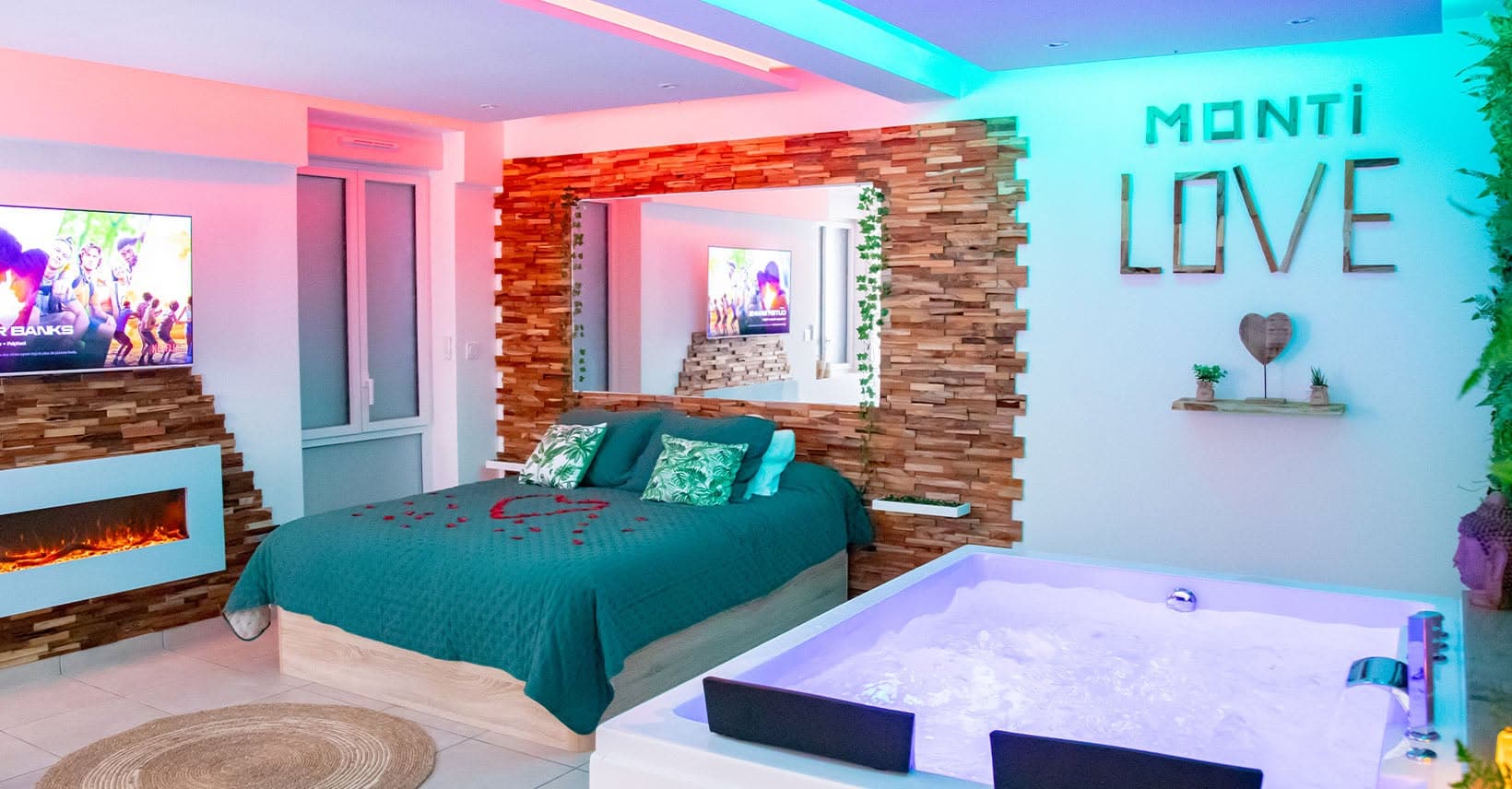 La love room Monti-Love à Montivilliers : lit double, baignoire balnéo et cheminée sous un éclairage d'ambiance