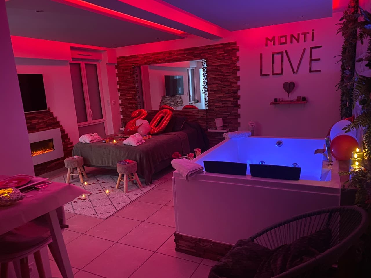 La love room entièrement décorée : lit, baignoire balnéo, ballons et table dressée